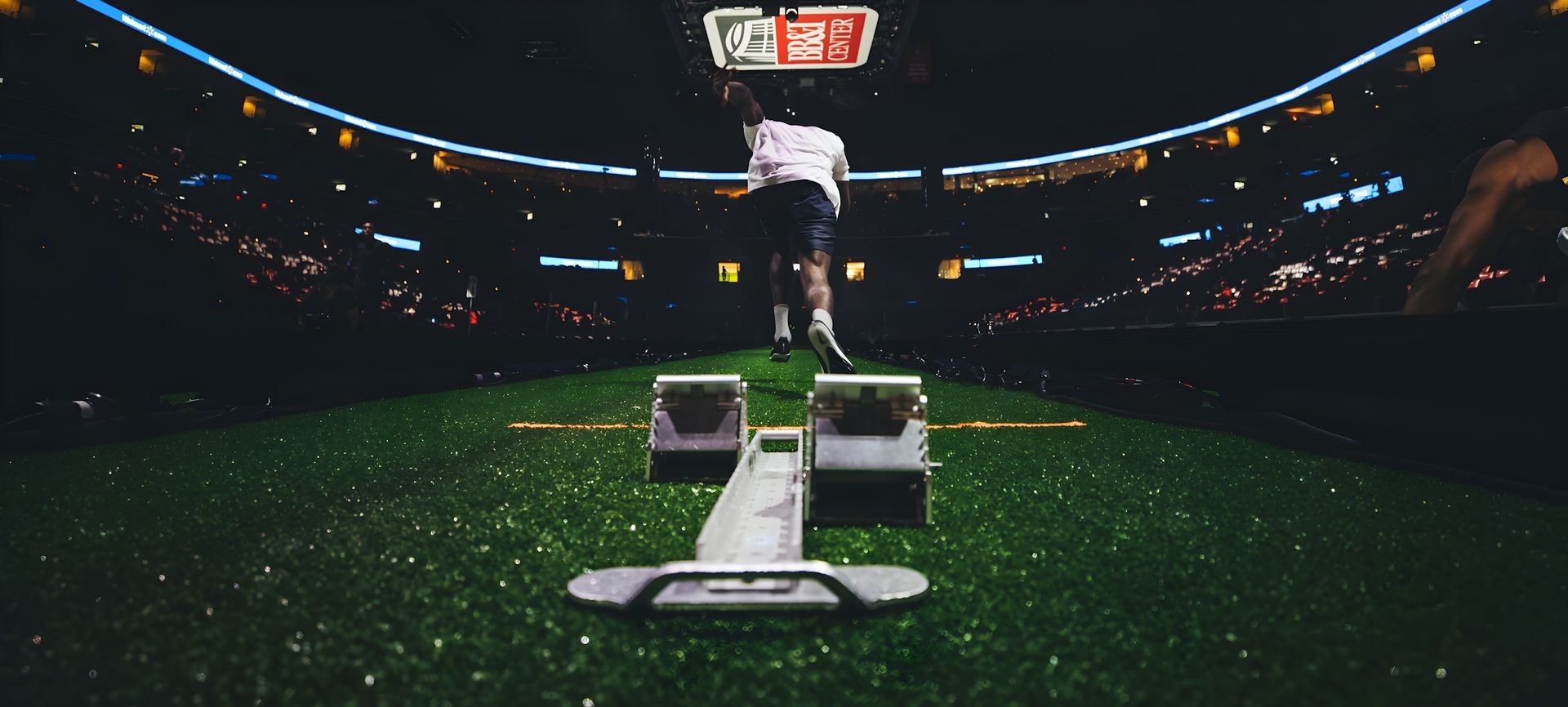 Athlete sprinting from starting blocks on a track in a stadium filled with spectators at night.